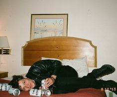 a man laying on top of a bed next to two beer cans in his hand