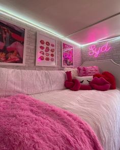 a bedroom with pink and white bedding, pictures on the wall and lights above it