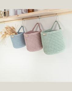 three crocheted baskets hanging from a wooden rack on a wall next to a shelf