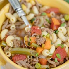 a yellow bowl filled with pasta, meat and veggies next to a spoon