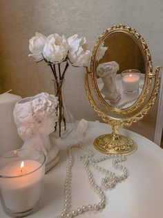 a white table topped with a gold mirror and pearls next to candles on top of it