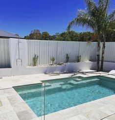 an empty swimming pool in the middle of a backyard with white walls and palm trees