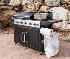 an outdoor grill with a roll of toilet paper on it and a large stone wall in the background