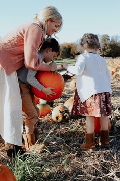 a woman and two children are picking up pumpkins