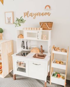 a playroom with white furniture and wooden shelves filled with toys, such as a toy kitchen