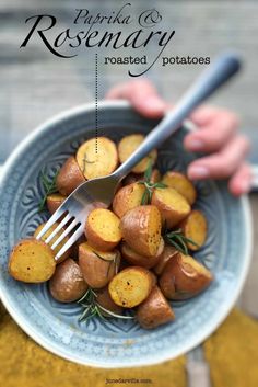 a person holding a fork in a bowl of roasted potatoes with rosemary on the side