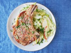 a white plate topped with meat and vegetables on top of a blue table cloth next to a fork