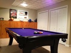 a pool table in a room with several balls on the floor and two doors behind it