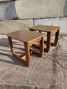 two wooden tables sitting next to each other on the ground in front of a stone wall