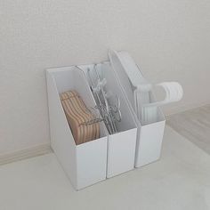 a white box with scissors and other items in it on the floor next to a wall