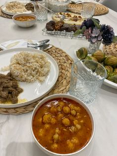 a table topped with plates of food and bowls of soup next to each other on top of a white table cloth