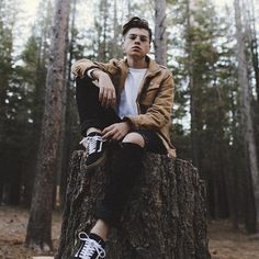 a young man sitting on top of a tree stump in the middle of a forest