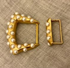 two pieces of gold and white pearls are sitting on a fabric surface, one is shaped like a rectangle