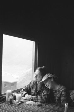 black and white photograph of two people sitting at a table looking out the window with mountains in the background