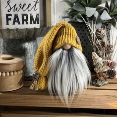 a small gnome with long white hair wearing a yellow knitted hat on top of a wooden shelf