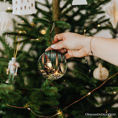 a hand holding an ornament in front of a christmas tree with ornaments on it