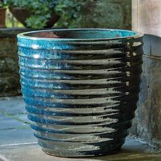 a large blue and black vase sitting on top of a cement floor next to a planter