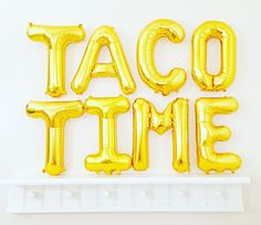 the word taco time spelled out with gold balloons in front of a white wall