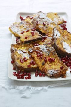 french toast with pomegranates and powdered sugar on a white plate