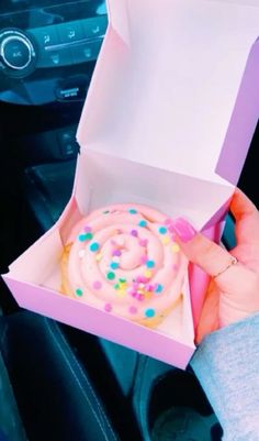 a person holding a pink box with a frosted donut in it