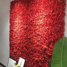 a red flowered wall hanging on the side of a white wall next to a green plant