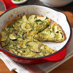 an omelet with zucchini and cheese in a red pan on a wooden table