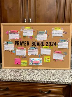 a bulletin board with notes on it in front of wooden cabinets and granite countertops