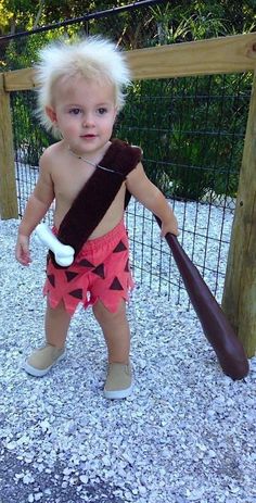 a toddler holding a baseball bat on top of gravel next to a wooden fence