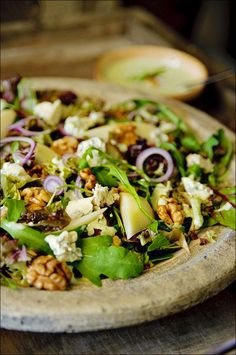 a salad with nuts and greens in a wooden bowl on a table next to an apple