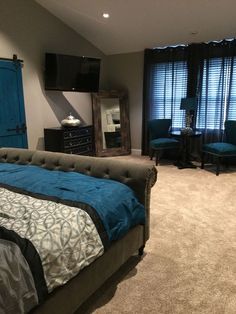 a bedroom with a bed, dresser and television on the wall next to two blue chairs