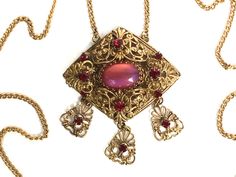 Czech Necklace with Pink Moon Stone Art Glass This exquisite necklace is from the 1920s or 1930s and is Czech. This piece is made of layers of beautiful ornate gold tone filigree in a large diamond shaped pendant. The center stone is a large oval pink cabochon of Czech art glass moon stone! The stone is gorgeous and glows from pink to purple catching the light in magically way. The center stone is surrounded by 8 deep garnet red rhinestones. The final touch is that there are 3 lovely filigree pendants each with  a garnet rhinestone hanging and dangling from the main pendant.  This piece is supported by a long gold chain which closes with a simples ring clasp. Chain Measures 23" long.  Pendant with dangles measures 2 3/8" x 2". This piece is in excellent vintage condition all metal and ston Vintage Eye Glasses, German Jewelry, Czech Jewelry, Filigree Necklaces, Silver Caps, Filigree Pendant, Pink Moon, Red Rhinestone, Moon Stone