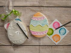 two decorated cookies sitting on top of a wooden table next to paintbrushes and paper