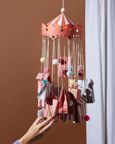 a person is holding an origami mobile in front of a curtain and window