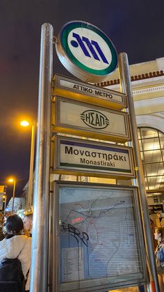 people are standing near a sign that says moscow metro station and it is lit up at night