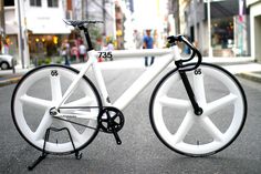 a white bicycle with black spokes parked on the side of a street in front of buildings