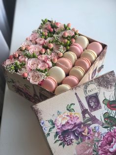 an open box filled with macaroons and flowers on top of a table next to a postcard