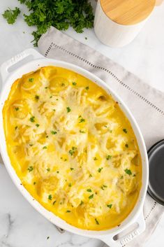 a casserole dish with cheese and parsley in it on a white table