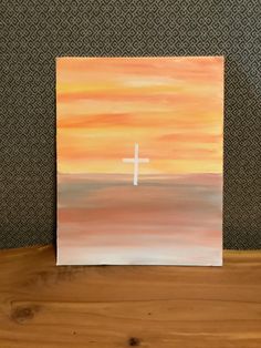 a painting with a cross on it sitting on top of a wooden table next to a wall