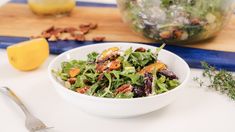 a white bowl filled with salad next to a knife and lemon wedge on top of a cutting board