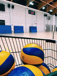 a shopping cart filled with blue and yellow volleyballs in a basketball court, indoors