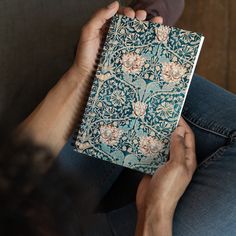 a person sitting on a couch holding a book in front of their face with both hands