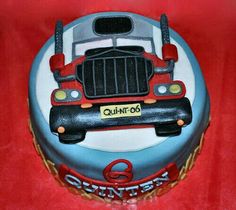 a birthday cake with a truck on the front and back of it, sitting on a red tablecloth