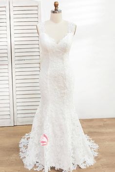 a white wedding dress on a mannequin in front of shutters and wooden floor