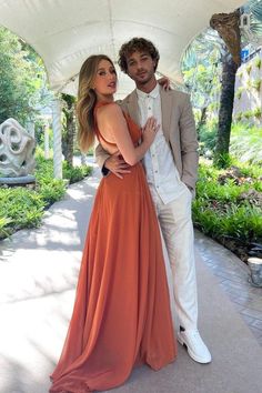 a man standing next to a woman in an orange dress under a white tent with palm trees