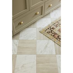 a bathroom with beige cabinets and white marble floor tiles on the floor, along with a rug in front of it