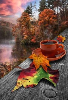 a cup of coffee sitting on top of a wooden table next to a fall leaf