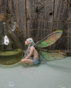 a fairy figurine sitting next to a glass jug with green liquid in it