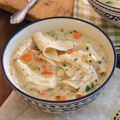 a bowl of chicken noodle soup on a napkin next to a wooden cutting board