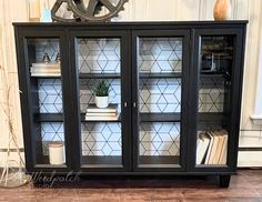 a black bookcase with glass doors and books on top is in front of a white wall