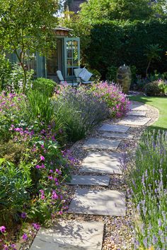 a garden with purple flowers and lavenders in the foreground, next to a stone path